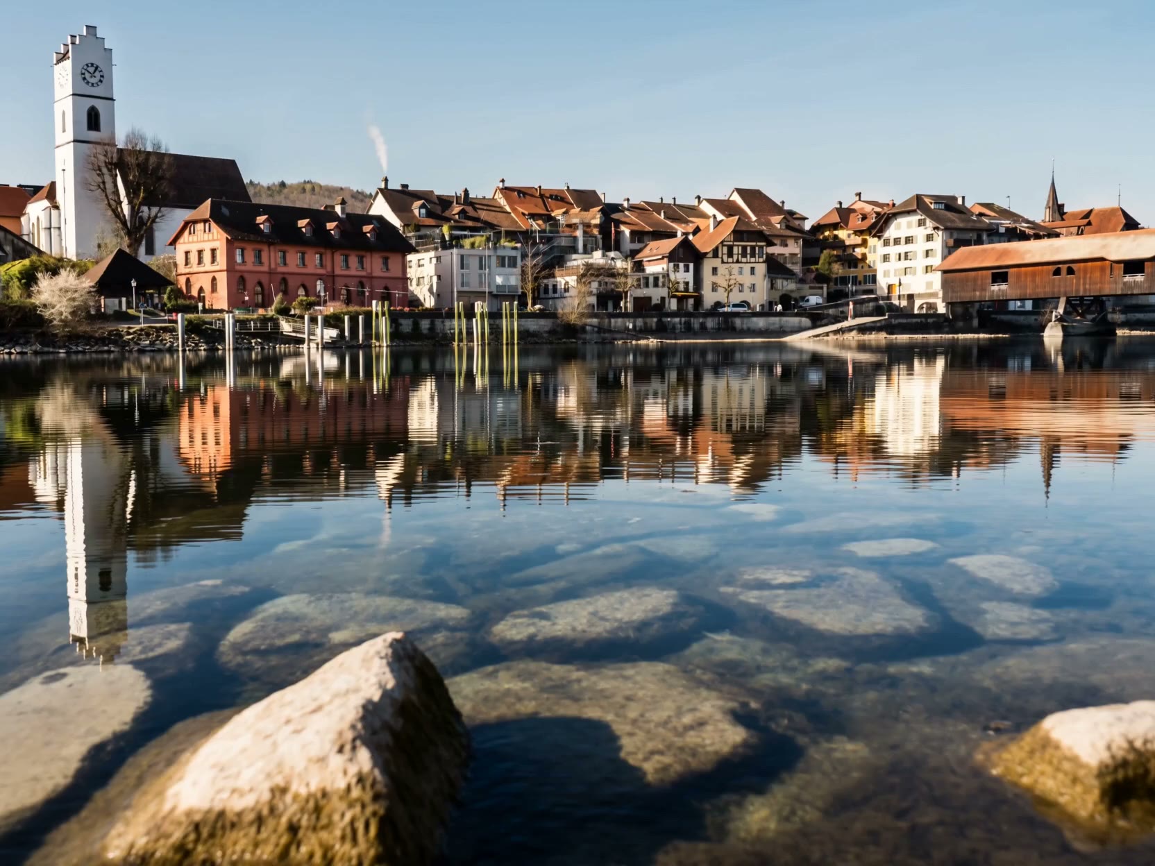 Die Altstadt von Büren an der Aare mit Kirchturm und gedeckter Holzbrücke, gespiegelt im Wasser
